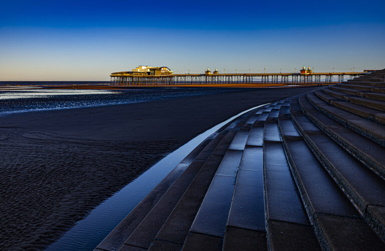 A vivid colourful sunrise on Blackpool beach.  Sharp winter sunlight painting shapes across the beach and piers.