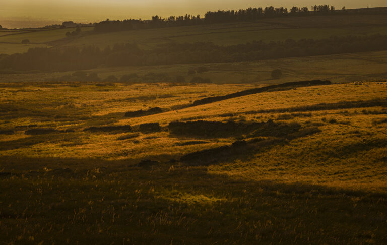 The last sunlight on a midsummers evening over the Pennine moors.  The wind farm and Blackpool tower are clearly visible on the coastline in the distance.  Warm light bathes the pennines making painting like pictures.