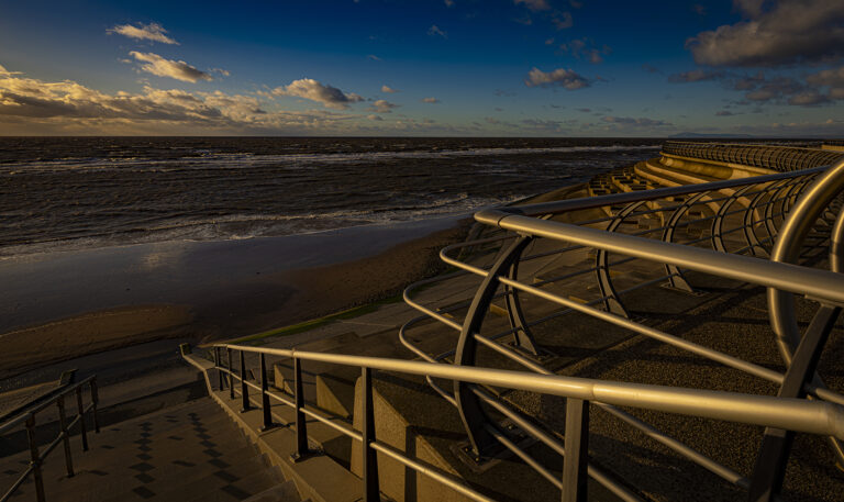 A very windy cold day on Blackpool prom.  Low sun in autumn picks out the rough sea and the defence structures.