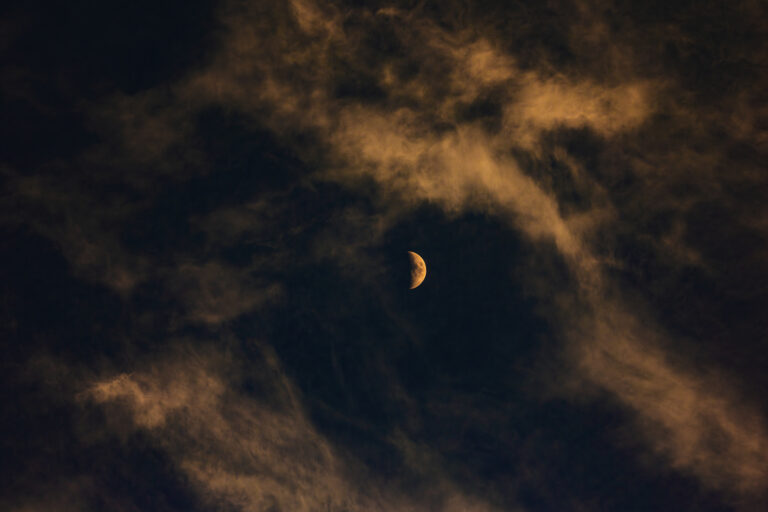Hazy evening clouds surround the moon which is illuminated by the setting son.