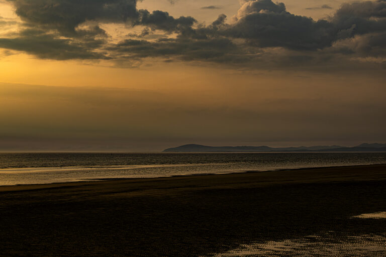 A very calm sunset reflected in a still sea.  The tide is receding creating channels across a deserted beach.