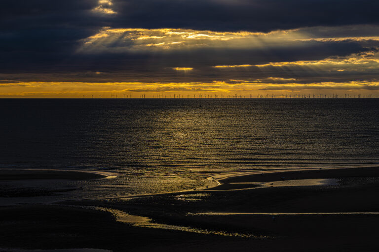 A very dramatic cloud filled sky as the sun sets over Anchorsholme in Blackpool.  The wind farm sits on the distant horizon as the tide slowly goes out.